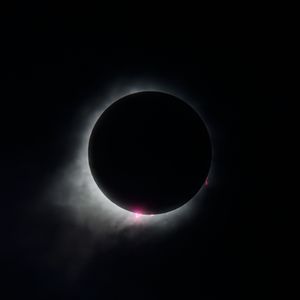 Total solar eclipse showing stunning corona and pink solar prominences against a dark sky.