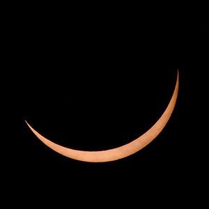 A crescent moon glowing orange against a dark black sky during a solar eclipse.