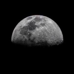A detailed close-up photograph of the half moon against a dark black sky showing craters and lunar surface.