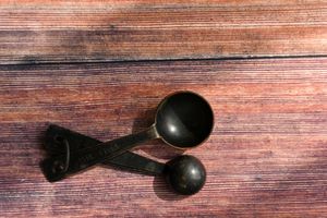Two vintage black measuring spoons resting on a rustic wooden surface.