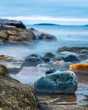 Rocky shoreline with smooth blue-grey stones and misty water creating a serene coastal landscape scene.