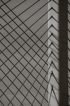 Abstract geometric pattern of diagonal metal wire fence casting shadows on gray wall surface.