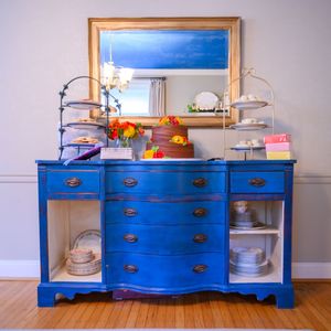 Vintage blue painted dresser with brass hardware, mirror, and decorative items on hardwood floors.