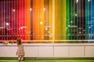 A young girl in a floral dress admires a vibrant rainbow-colored display wall at an interactive museum exhibit.