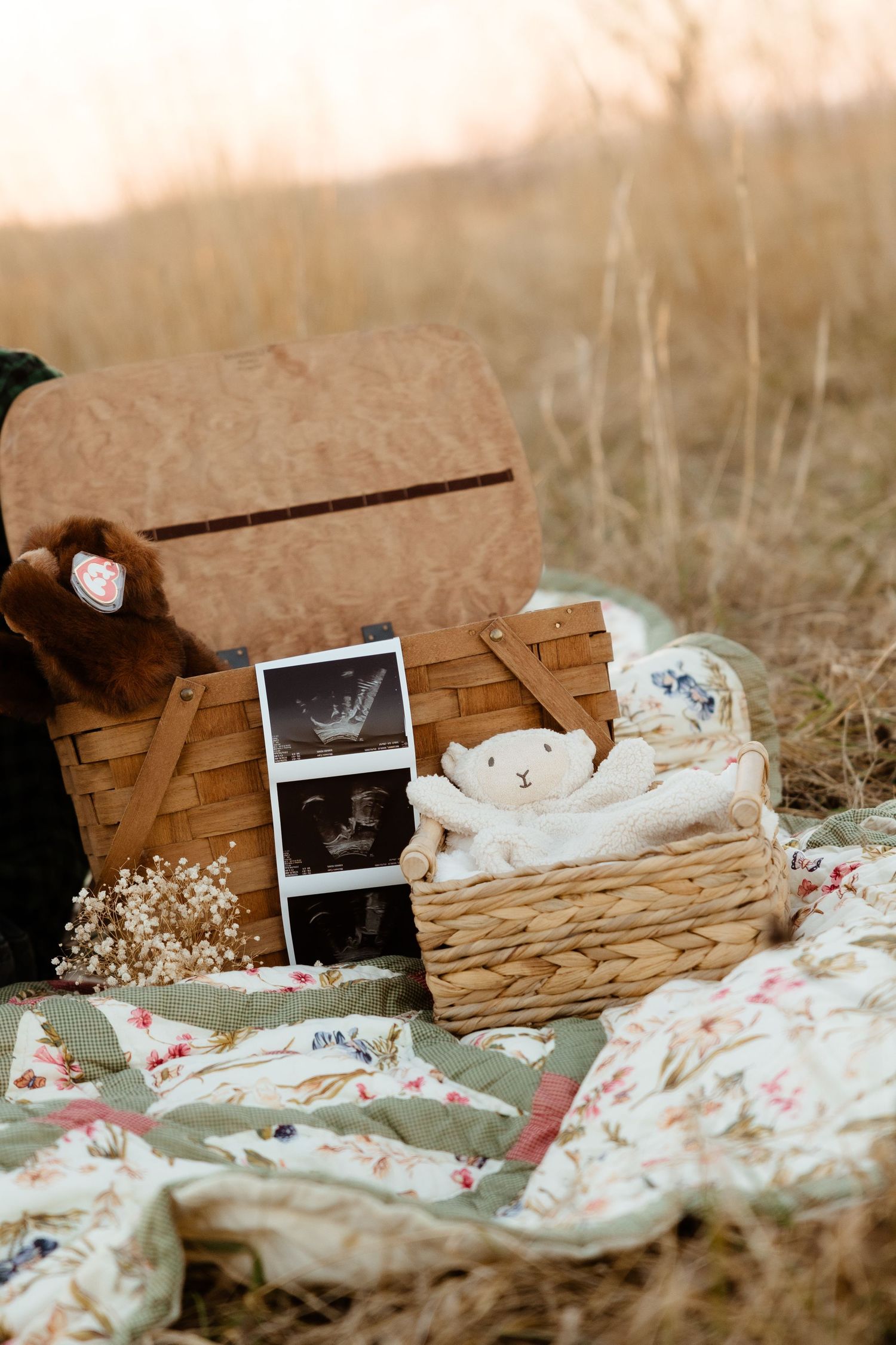 A warm maternity flat lay featuring ultrasound photos, baby toys, and a wicker basket on a floral quilt.