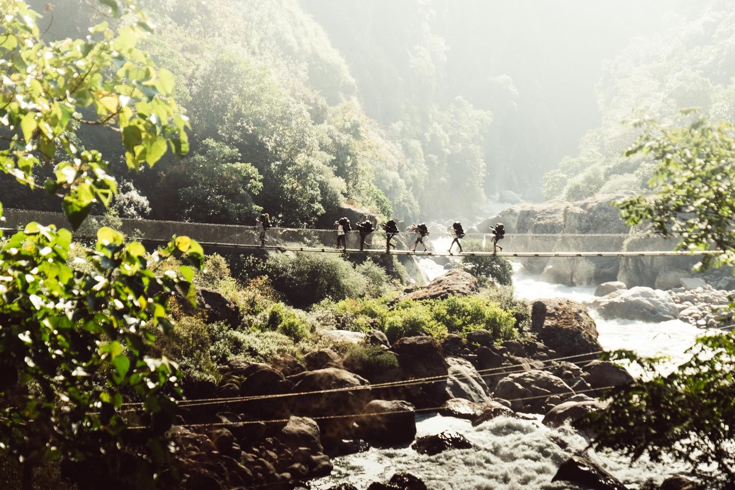 Misty mountain landscape with people crossing bridge over rushing river.