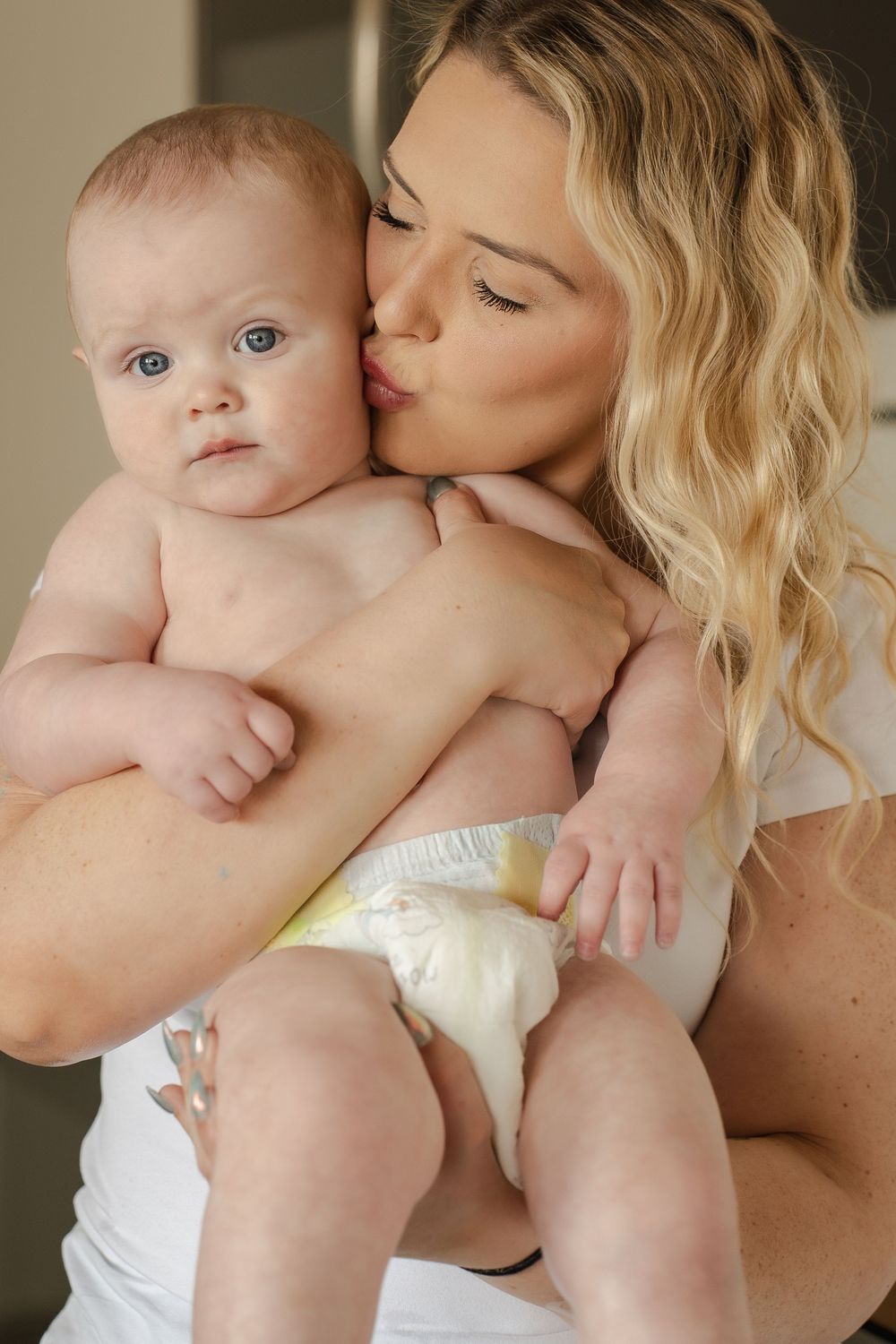 A tender moment between parent and baby in white, with soft natural lighting and gentle embrace.