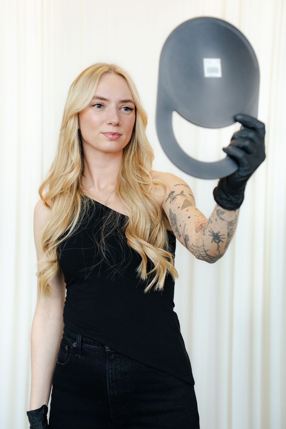 A person wearing a black outfit and gloves poses in three similar shots against a white curtain background.