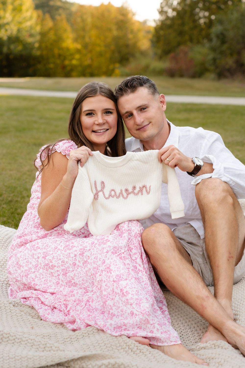 Romantic couple lounges together on blanket outdoors wearing pink floral dress and white shirt.