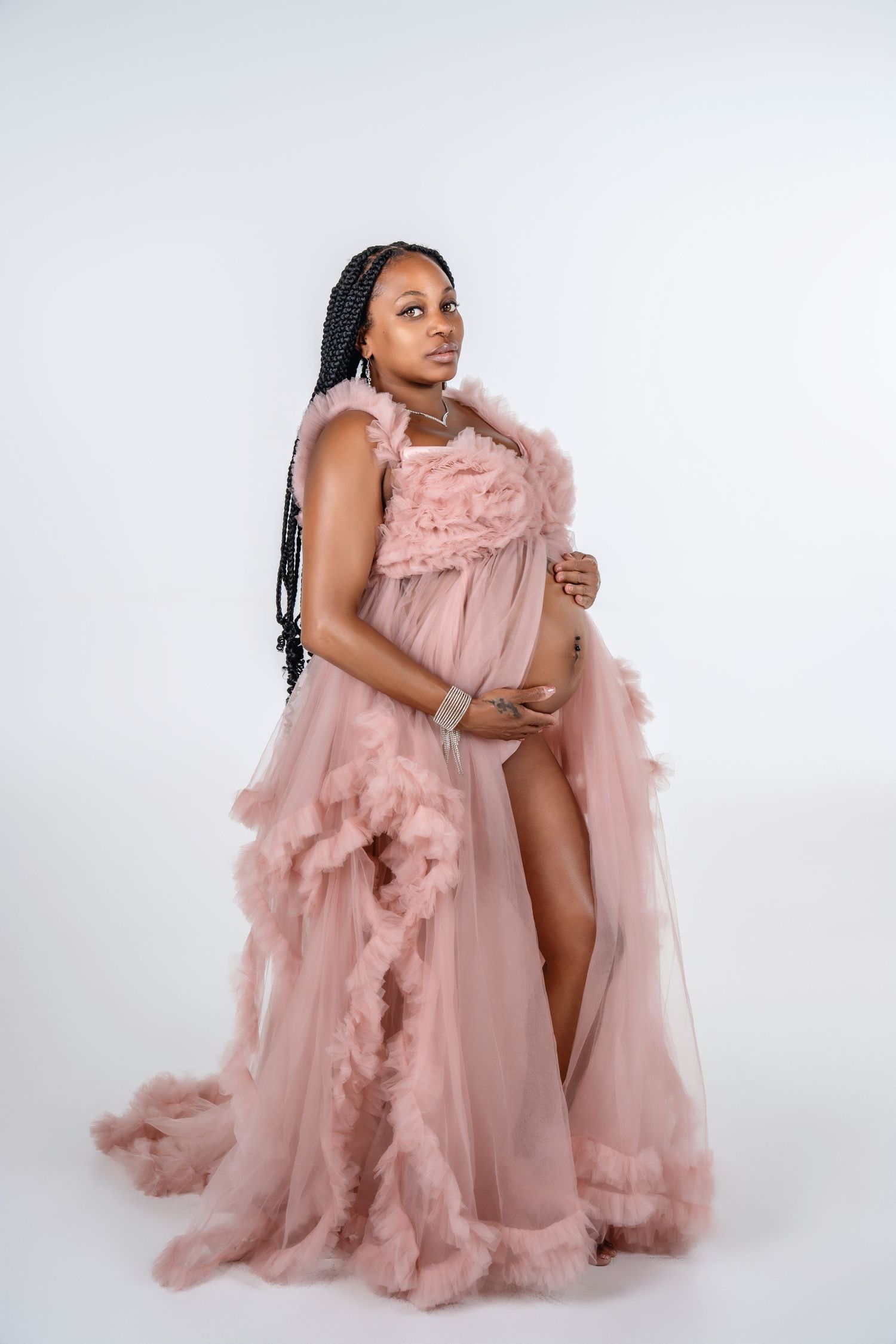 Elegant maternity photo featuring a sheer pink ruffled gown against white background.