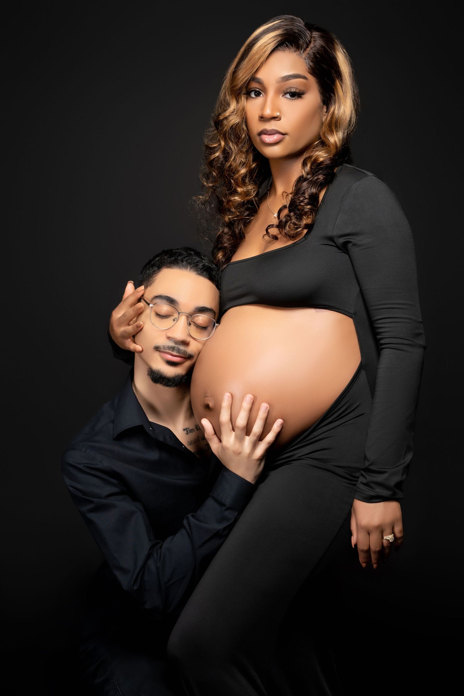 Intimate black and white studio maternity portrait with couple in dramatic lighting.