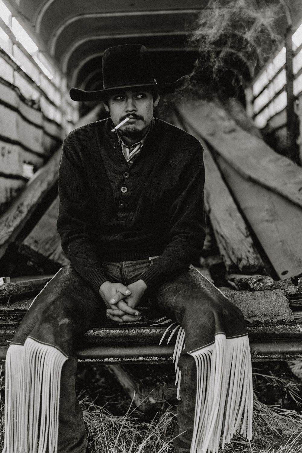 Dramatic black and white portrait of person in western attire with smoke effects in cattle trailer.