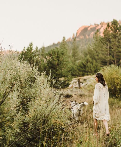 Dreamy outdoor scene with white dress against mountain landscape and pine trees.