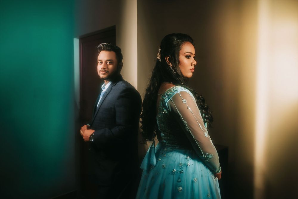 A couple in formal wear poses dramatically in a room with turquoise and amber lighting.