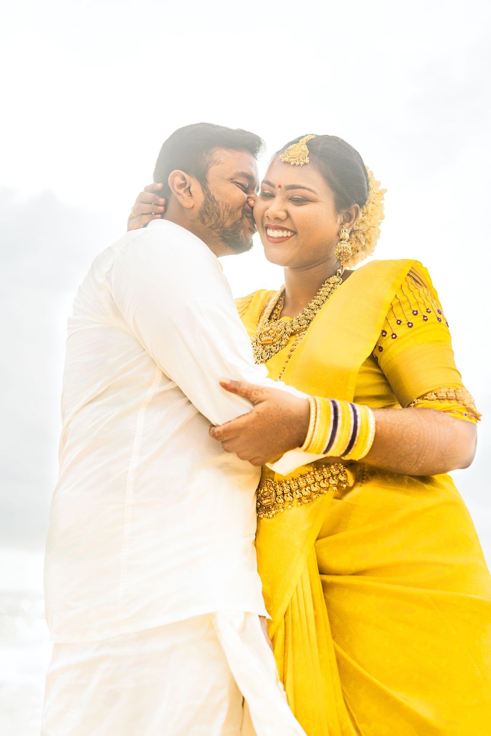 A couple shares a tender moment outdoors, with one wearing a vibrant yellow sari and gold jewelry.