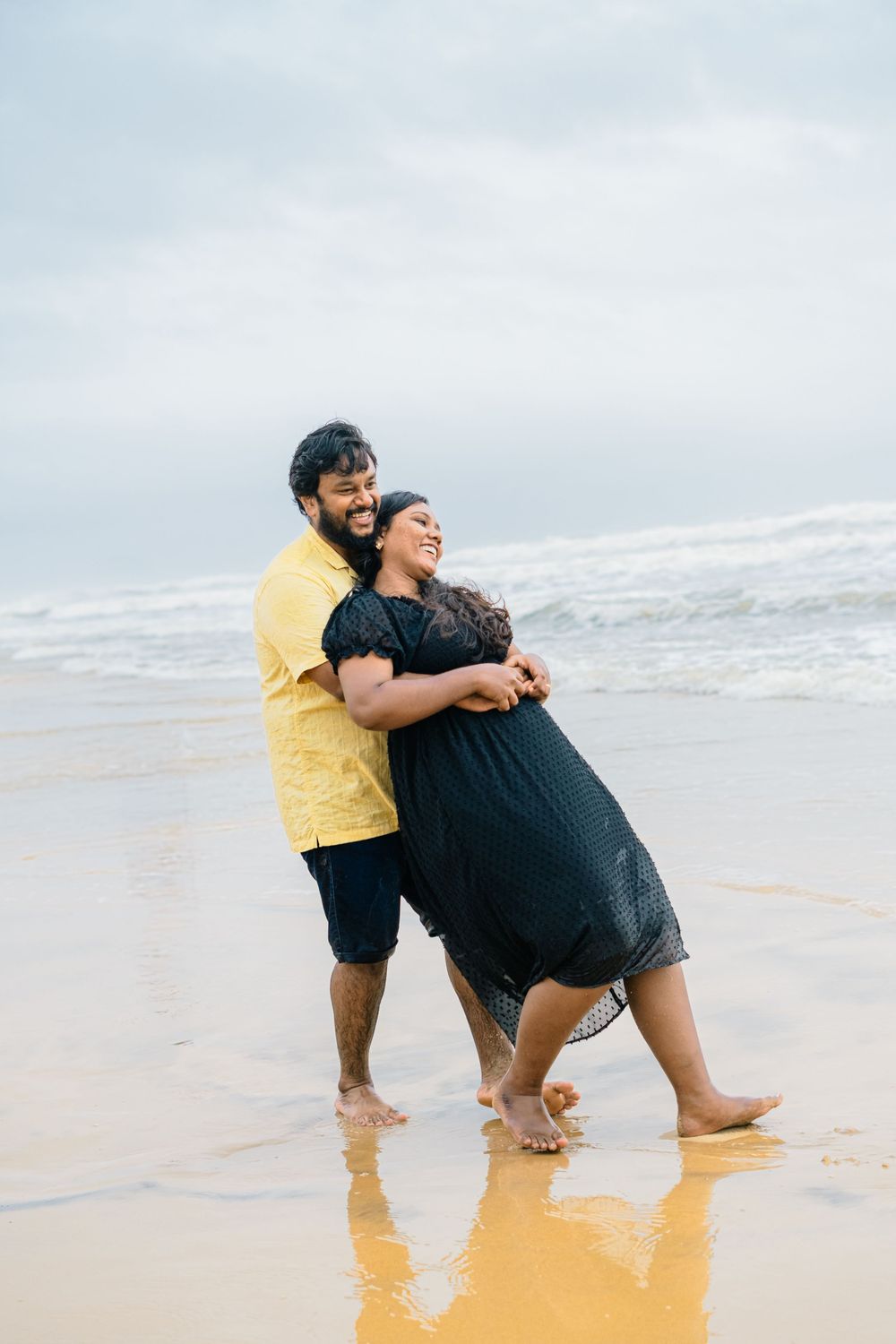 Joyful couple embracing and laughing together on a beach at sunset.