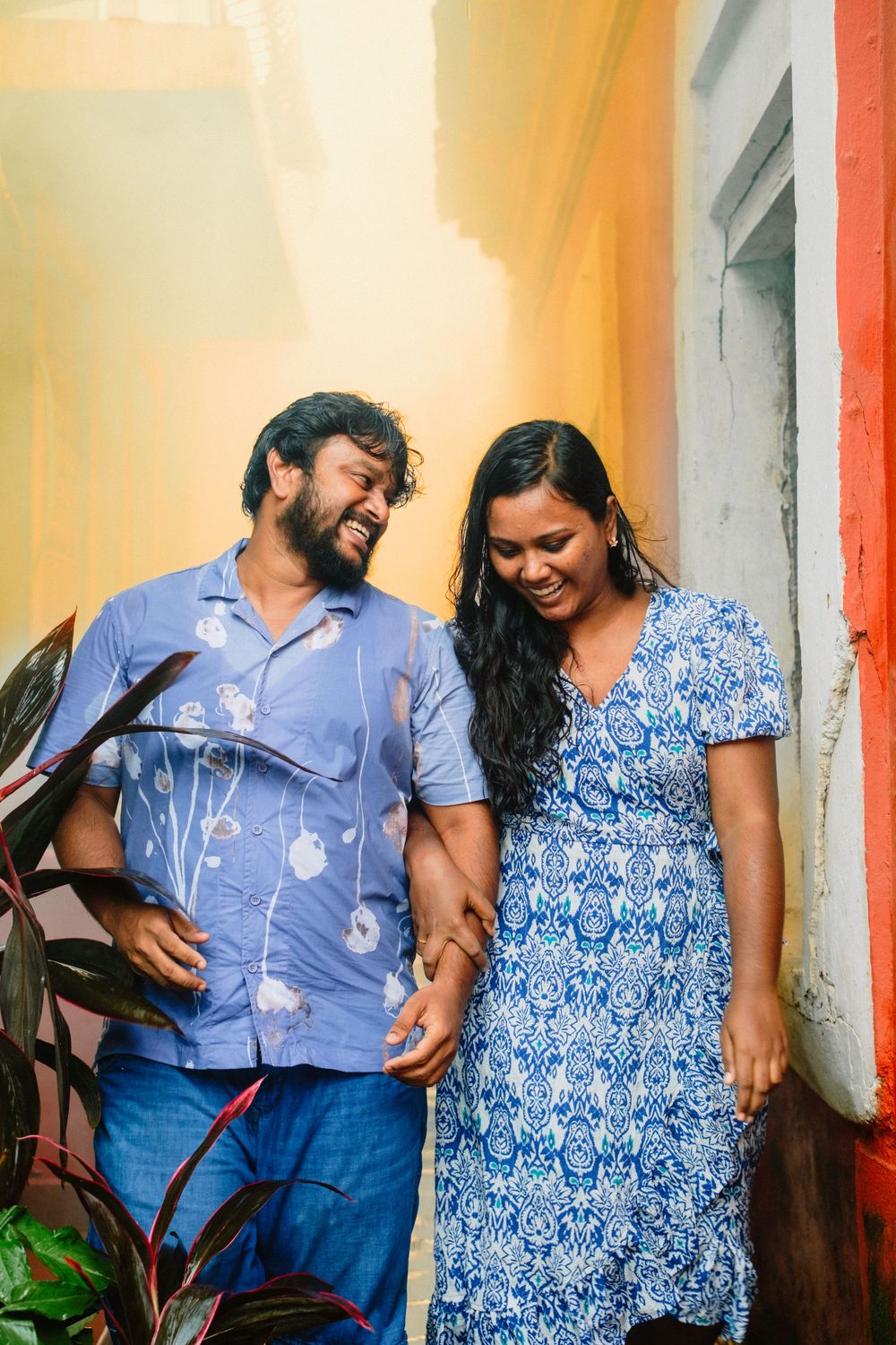 Happy couple in coordinated blue outfits sharing a laugh in front of yellow wall.