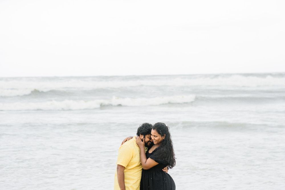 Romantic beach portrait of couple embracing with ocean waves in background.