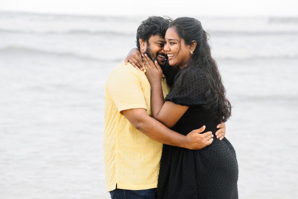 Couple in yellow and black sharing intimate embrace on cloudy beach.