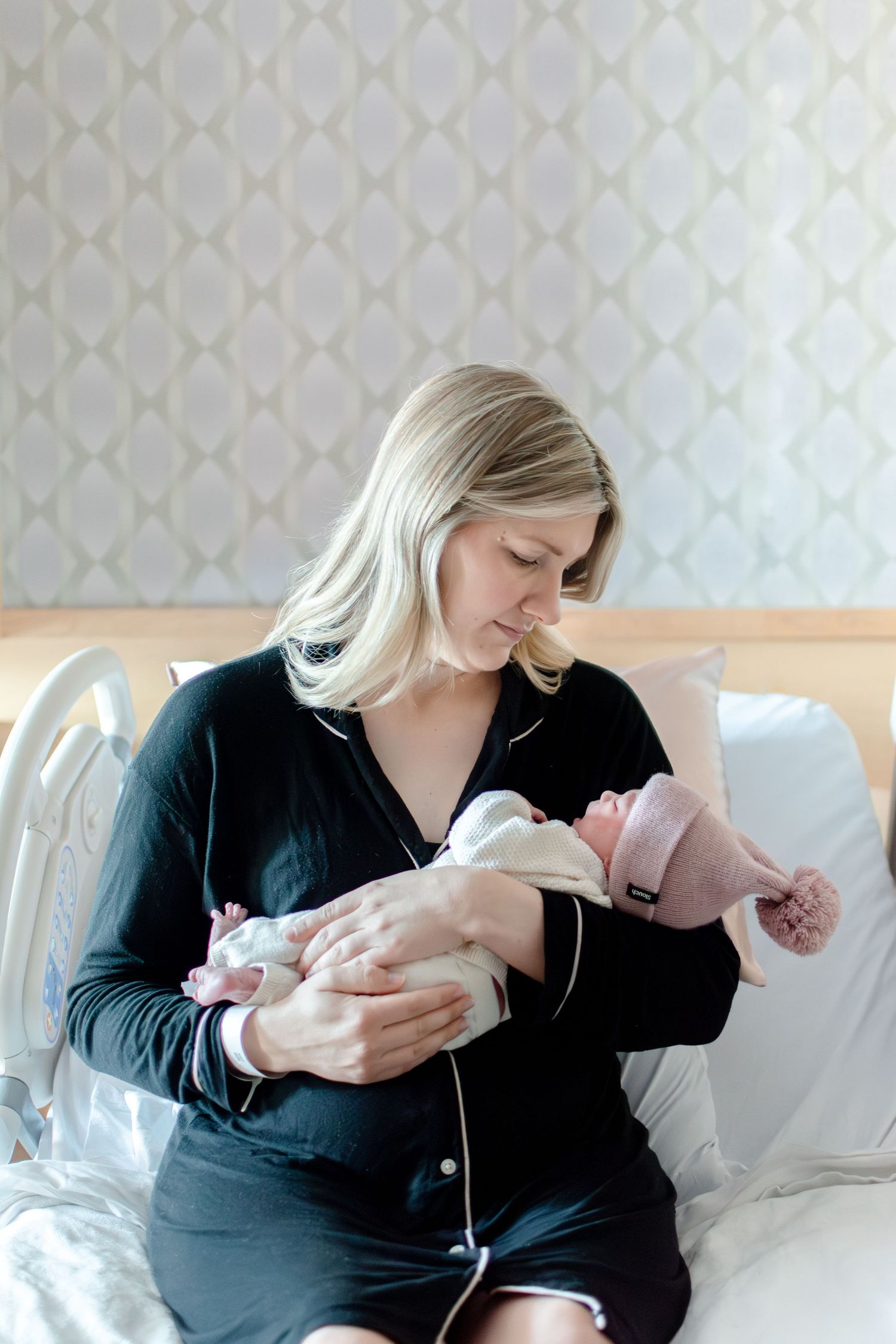 Intimate moment between parent and newborn in a cozy room with patterned wallpaper.