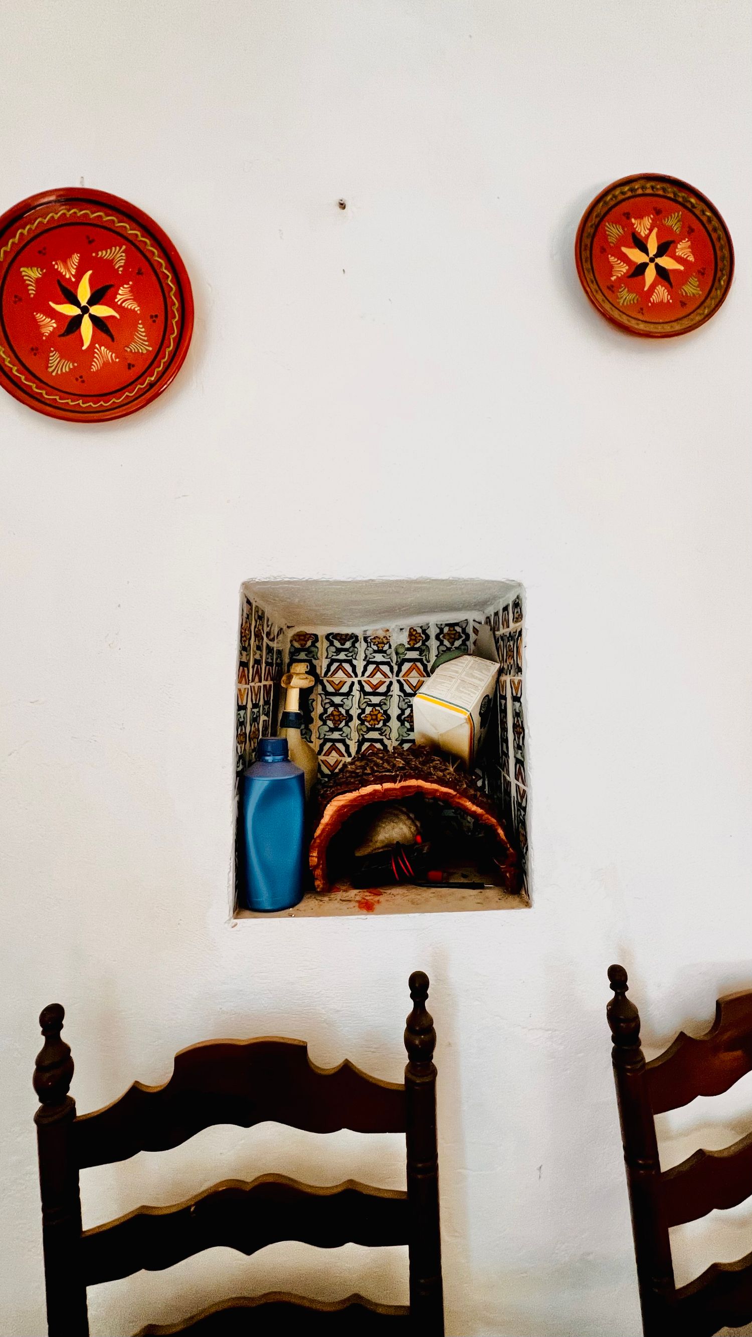 Decorative red plates with gold star patterns hang above wooden chairs against a white wall in a rustic interior setting.