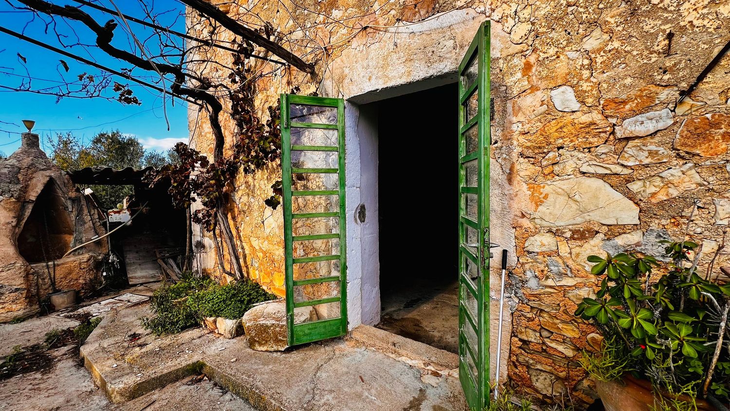 A weathered stone wall with green wooden doors and windows creates a rustic Mediterranean architectural scene.