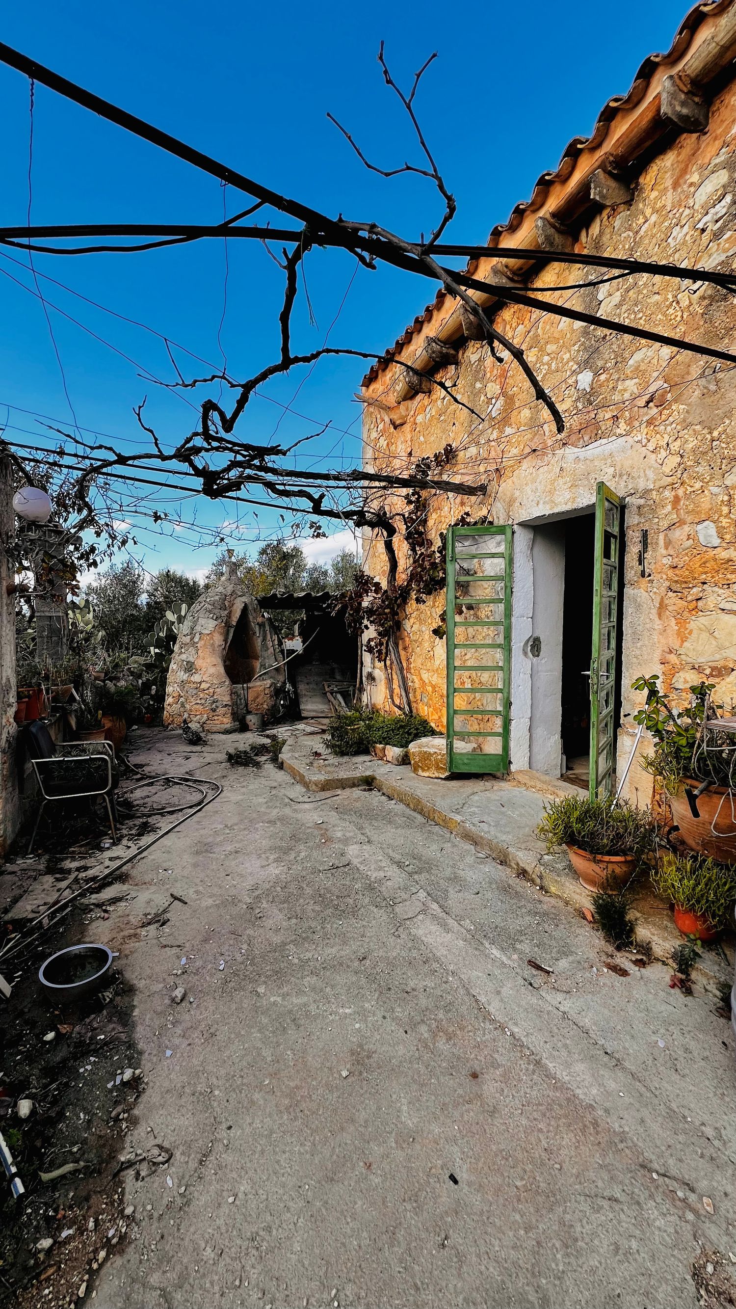A narrow cobblestone alley with rustic stone walls and green doors leads through a Mediterranean village on a sunny day.
