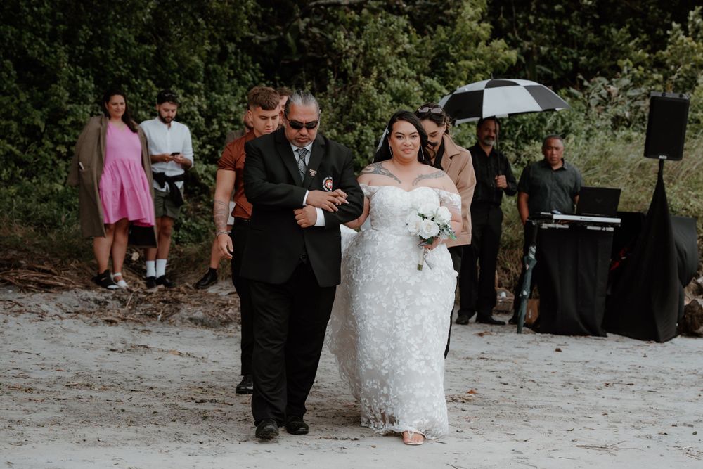Coastal beach wedding ceremony with couple walking down sandy aisle.