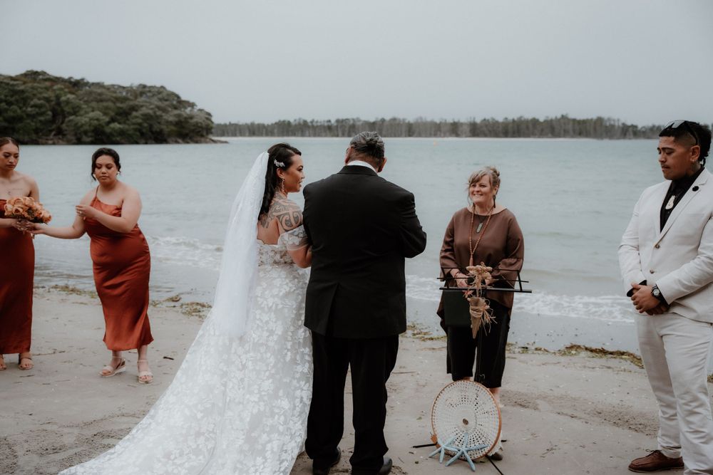 Beachside wedding ceremony with officiant and guests gathered on sandy shore.