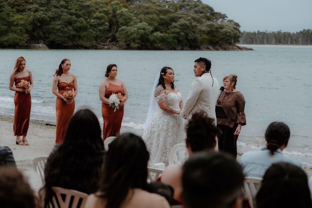 Wedding ceremony set against ocean backdrop with bridesmaids in rust-colored dresses.