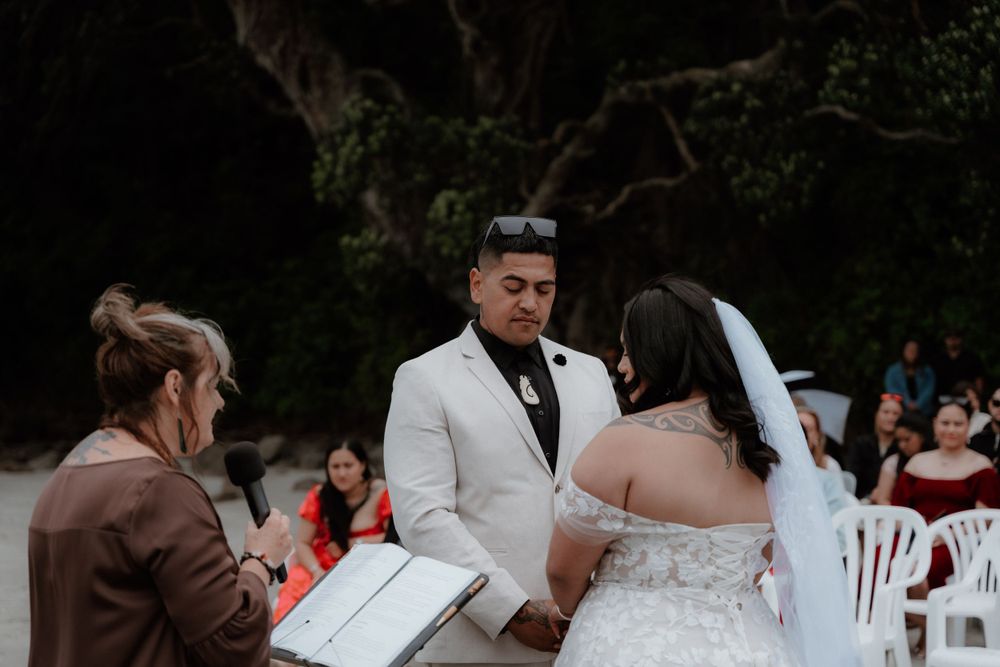 A waterfront wedding ceremony with attendees in white chairs as the couple stands with the officiant.