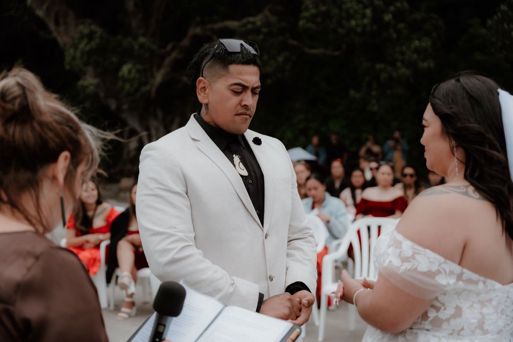 An intimate beachfront wedding ceremony with guests watching the couple exchange vows.