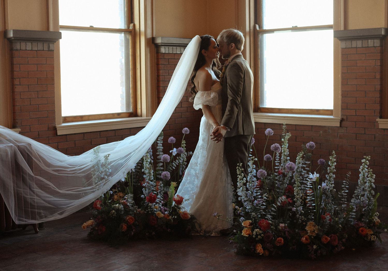Flowing white wedding veil draped elegantly near windows with floral arrangements.