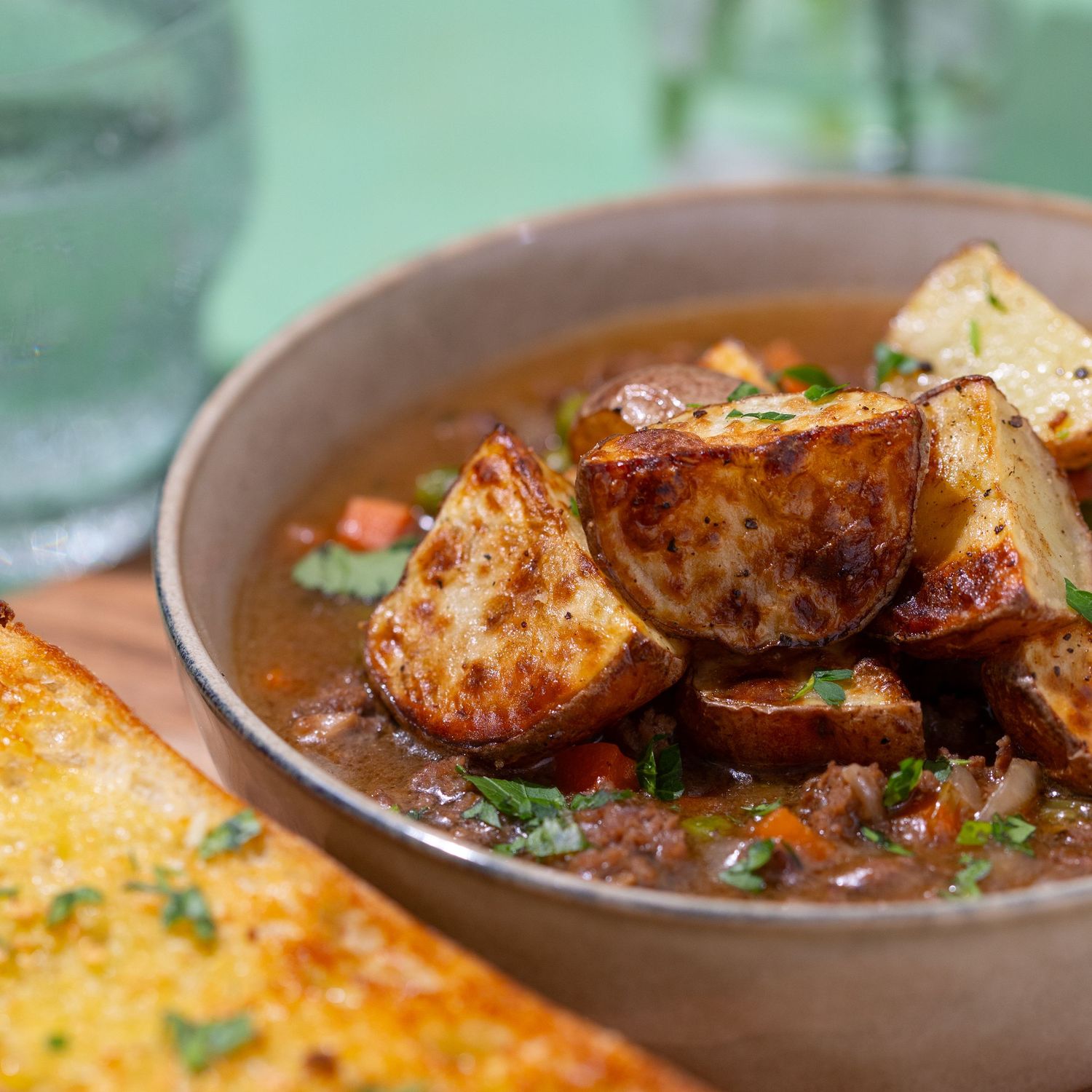Overhead view of spicy roasted potatoes garnished with fresh herbs in a rustic brown serving bowl.