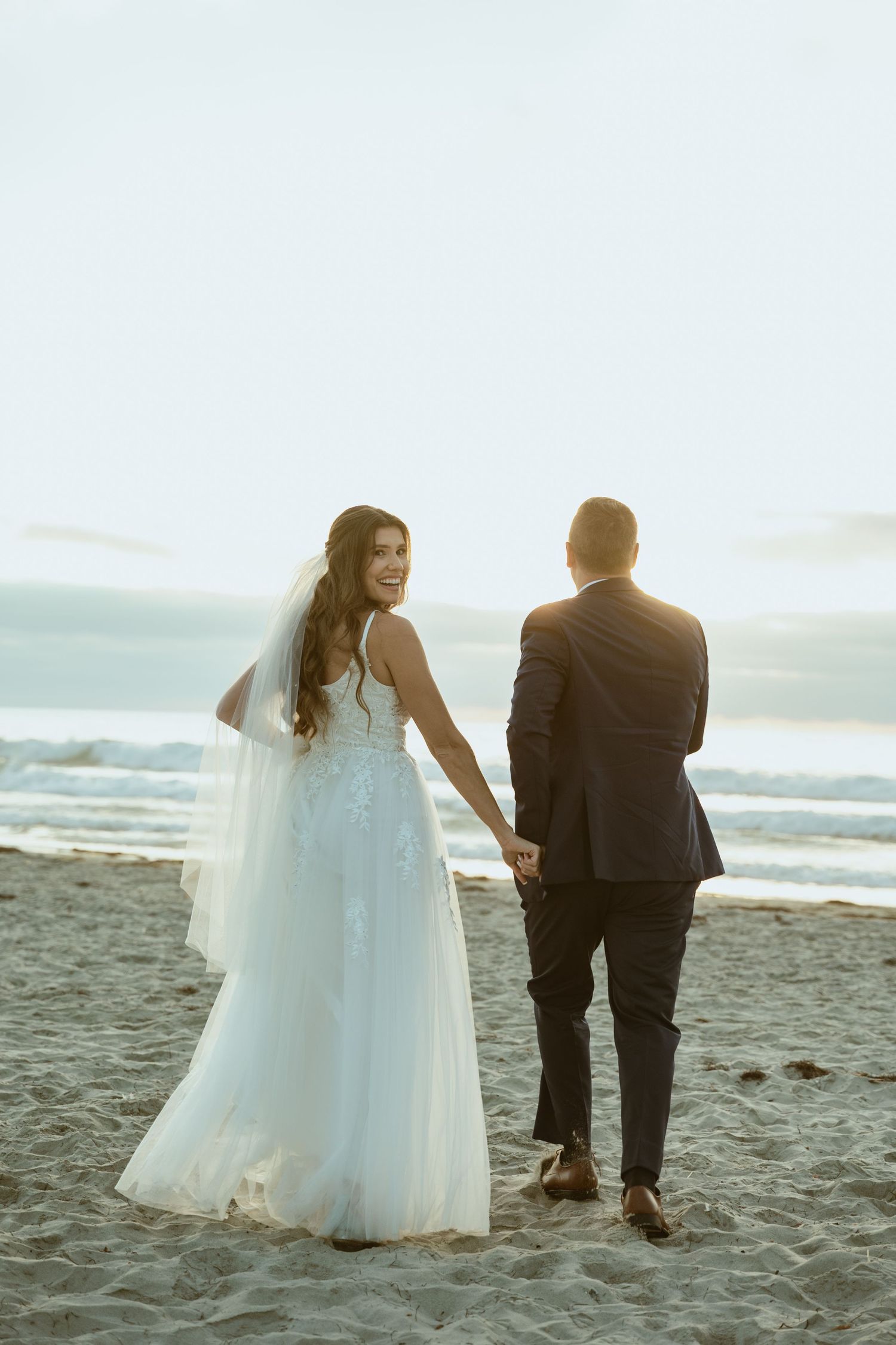 Romantic beach wedding photo of couple standing together on sandy shore.