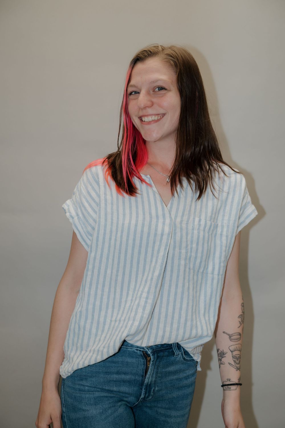 A casual portrait featuring a striped button-down shirt and red-streaked hair against a neutral background.