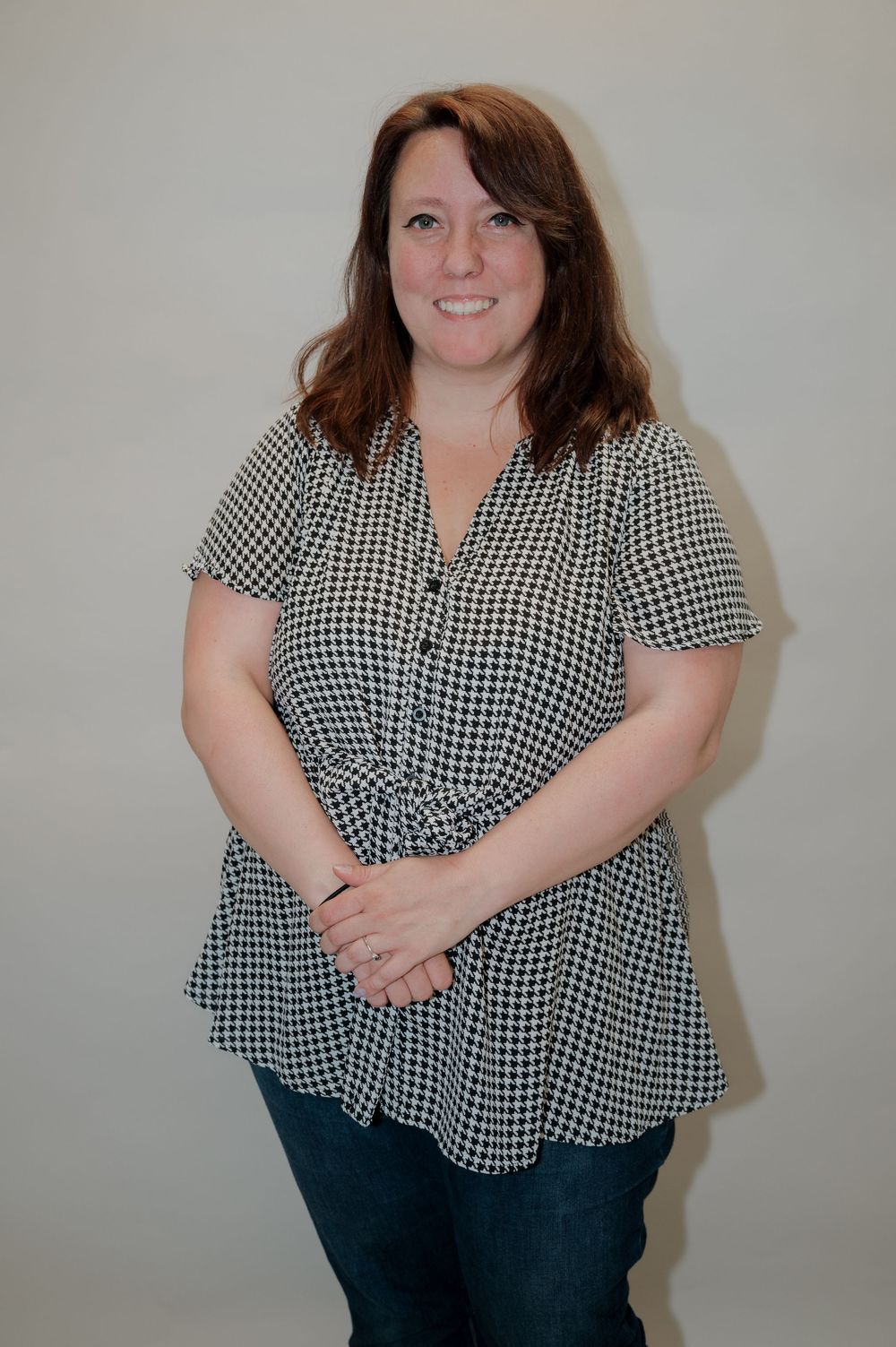 Woman wearing black and white gingham pattern blouse posing against light background.