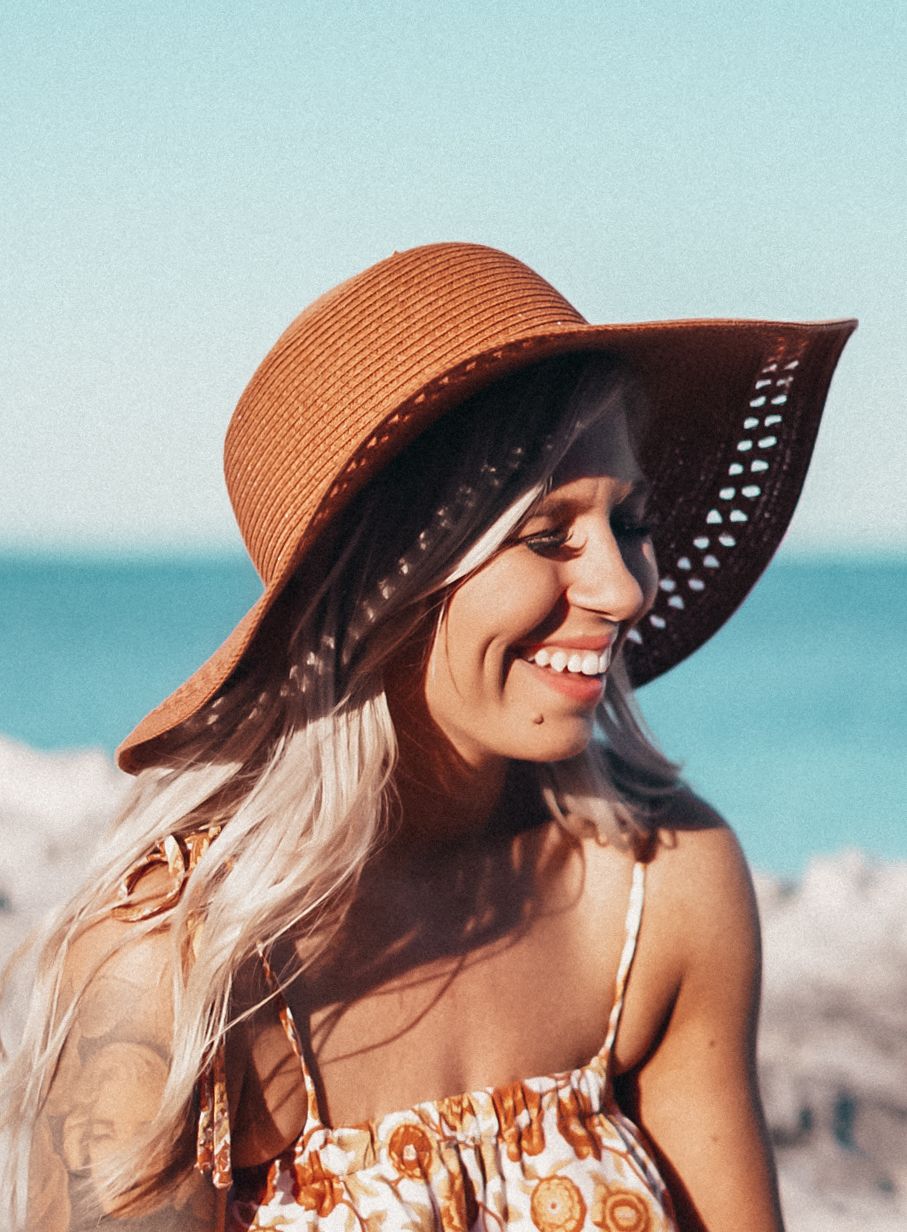 Smiling woman wearing a brown straw sun hat at the beach on a sunny day.
