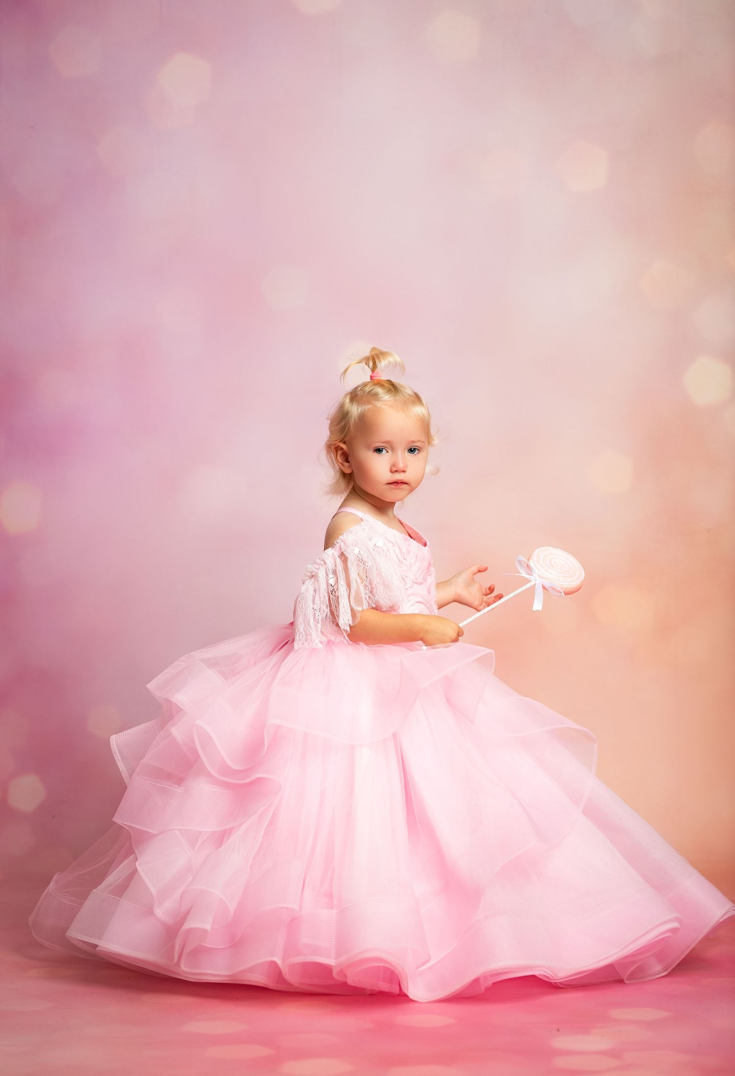 Young girl wearing a flowing pink princess ball gown with tulle skirt against a textured brown backdrop.