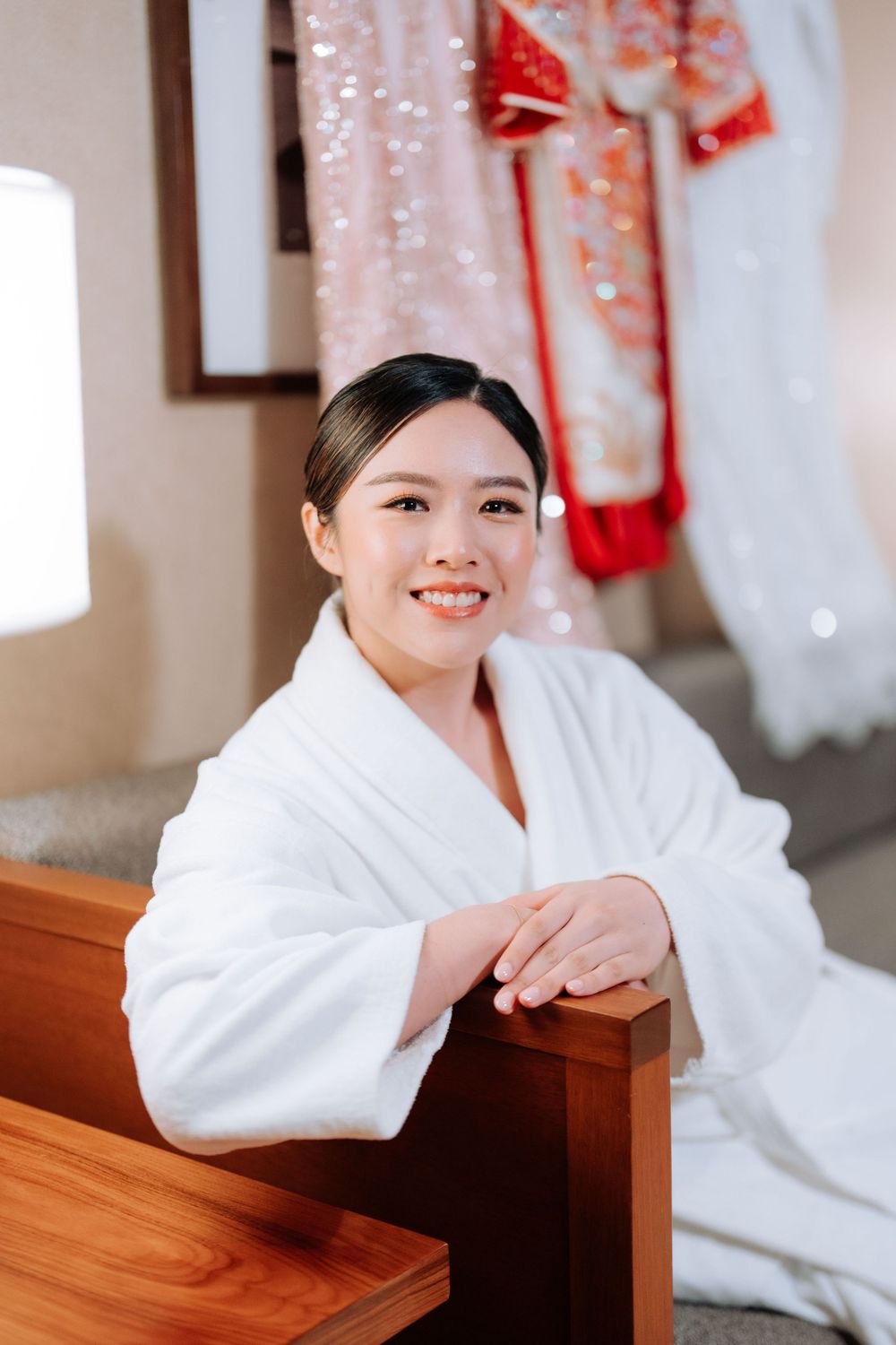 Person in white bathrobe sitting in hotel room with traditional wedding attire displayed in background.