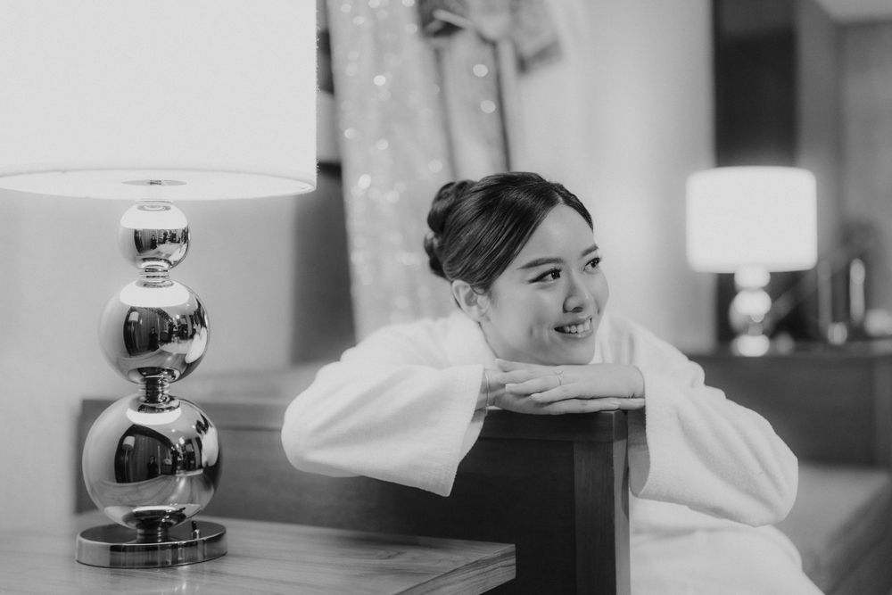 Black and white portrait of person in white robe resting on wooden furniture.