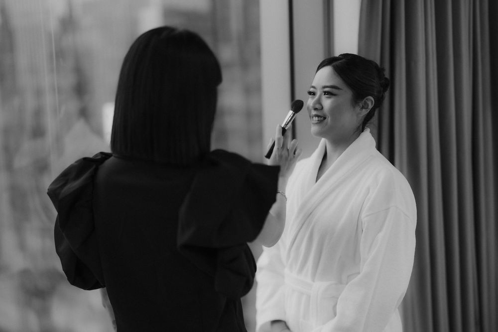 Black and white photo of makeup application session during wedding preparations.