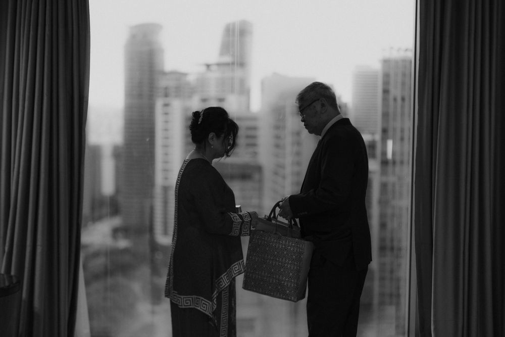 Black and white silhouette of two people by window with cityscape view.