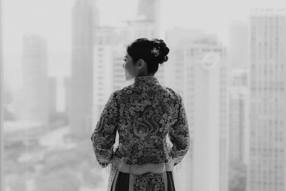 Black and white photo of person in patterned dress looking at city skyline through window.