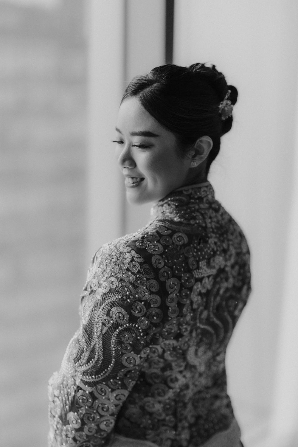 A black and white portrait of a person in a lace dress smiling with their eyes closed.