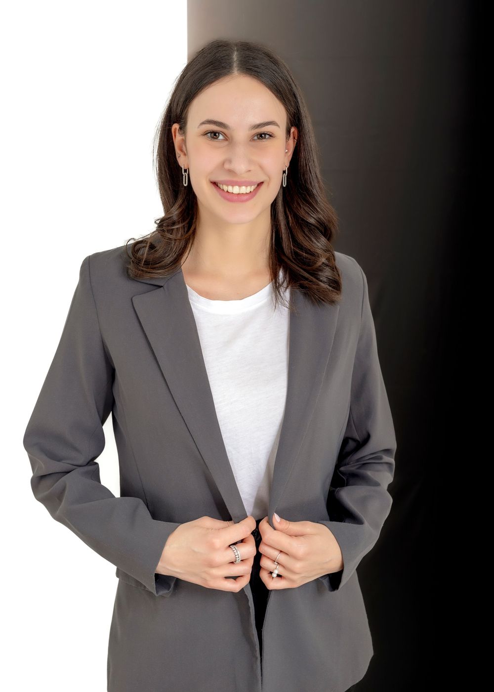 Bewerbungsfoto einer jungen Frau mit langen dunklen Haaren in einem klassischen Blazer vor einem zeigeteilten Hintergrund  im Fotostudio