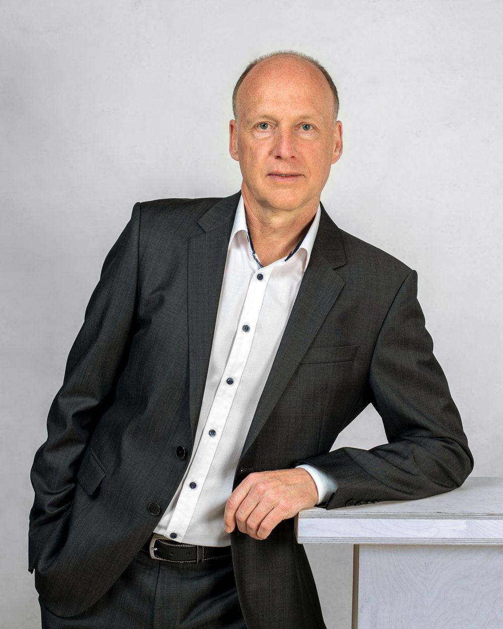 Professionelles Businessfoto eines Mannes in einem grauen Anzug aufgestützt auf einem Pult wie ein Redner lässig aber bestimmend