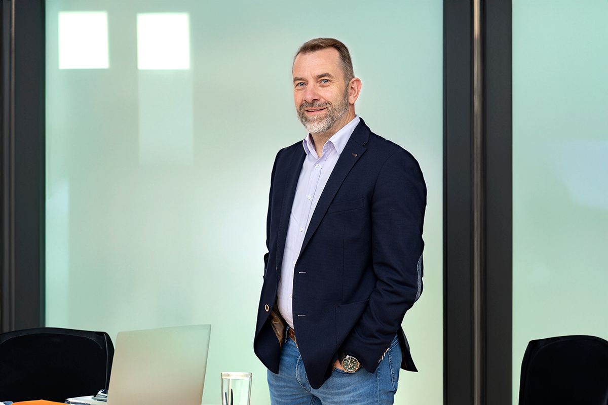 Businessfoto eines Mannes mit Bart vor einer Glaswand in einem Büro