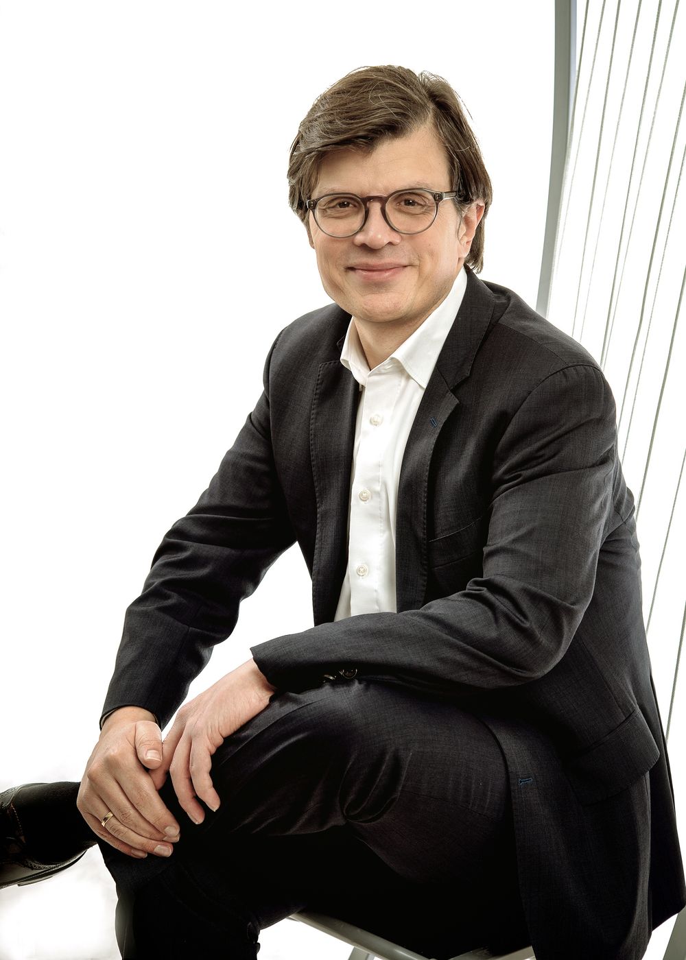 Professional wearing a black suit and glasses poses in four similar seated positions against a white background.