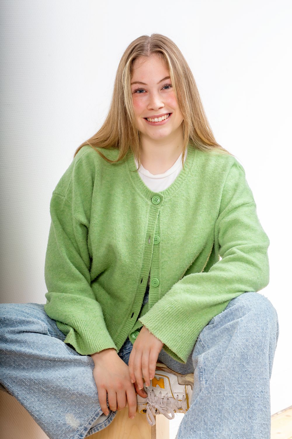 lässiges Bewerbungsfoto einer jungen Frau, die auf einer Box sitzt ein Bein untergeschlagen und aufgeschlossen lächelt Diemelstadt
